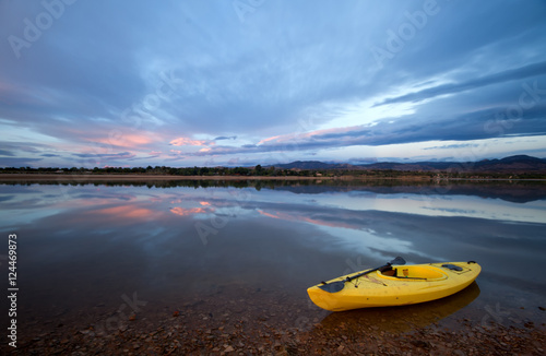 One Yellow Kayak with an oar on the shore of a lake at sunrise