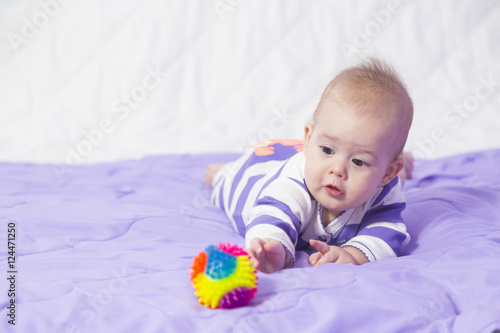 A six month old baby girl lying on stomach and holding the ball .