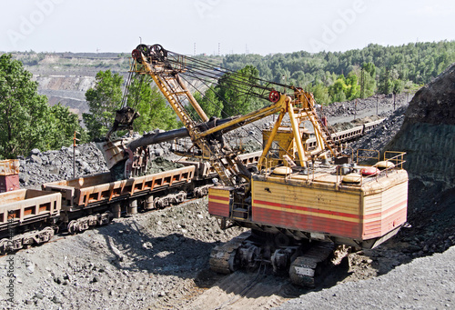 Excavator loading iron ore into goods wagon on the iron ore opencast mine