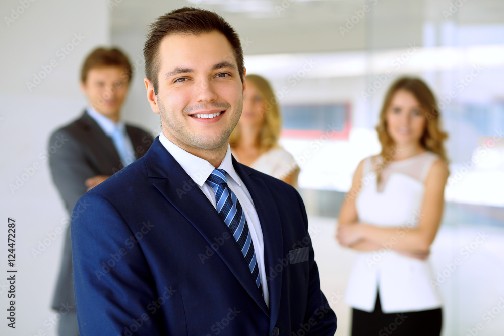 Smiling businessman in office with colleagues in the background Smiling businessman in office with colleagues in the background