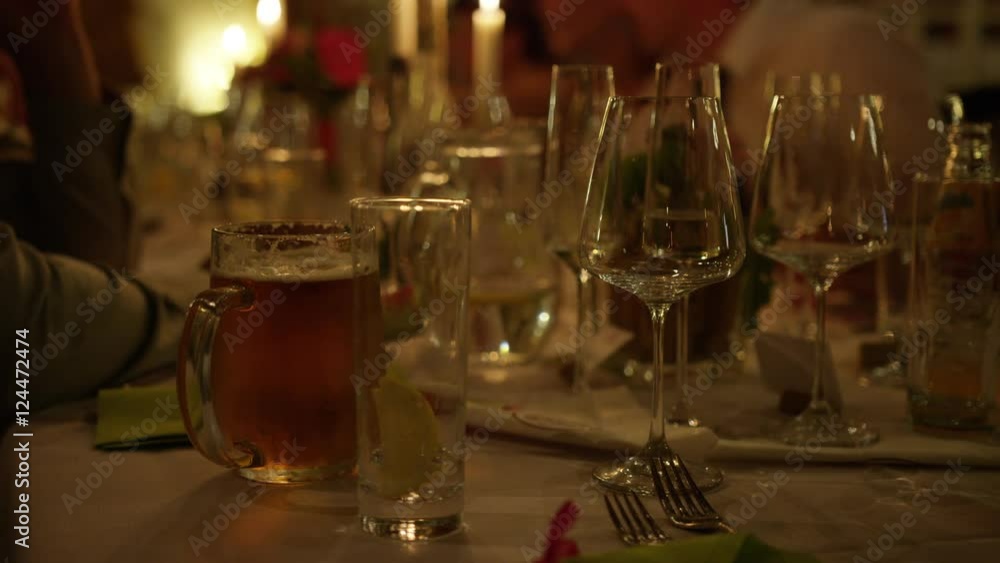 A candlelit table during a wedding reception in Moravia, Czech Republic. Table is filled with wine glasses and a full beer mug. The blurry torsos of guests are visible. 4k. A candlelit table during a wedding reception in Moravia, Czech Republic. Table is filled with wine glasses and a full beer mug. The blurry torsos of guests are visible. 4k.