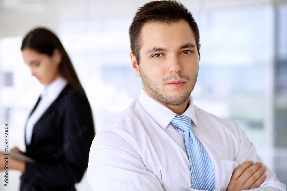 Smiling businessman in office with colleagues in the background Smiling businessman in office with colleagues in the background