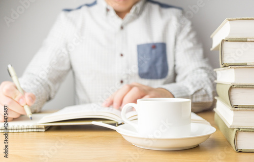 A man reading and making notes with a cup of coffee on the table
