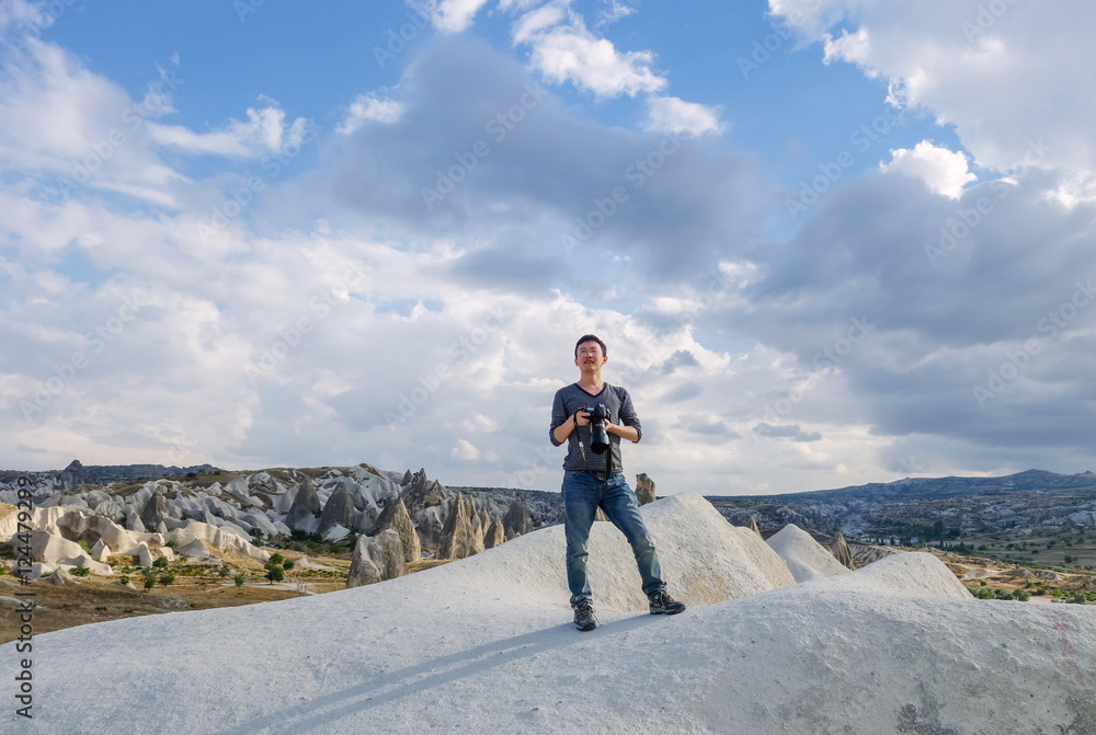 Obraz premium young man taking photo of landscape, standing on rocks in Goreme National Park, typical terrain landscape in Cappadocia, Turkey