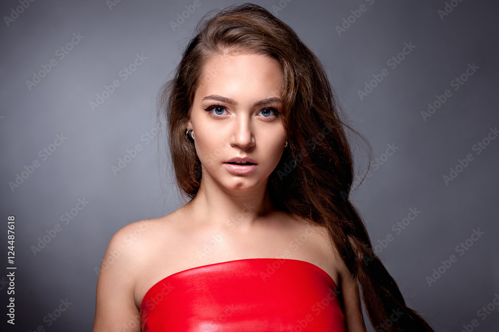 Portrait of the teenager in a red dress on a gray background