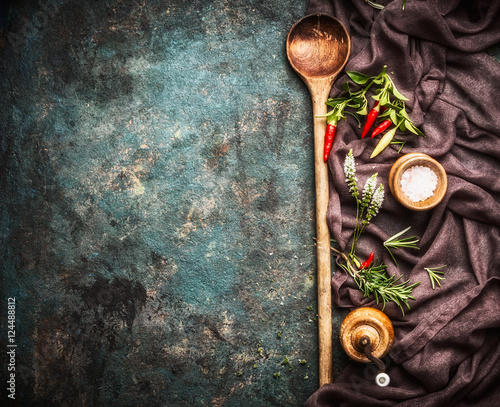 Food background with old wooden cooking spoon , napkin , spices and flavoring on dark rustic background, top view, border