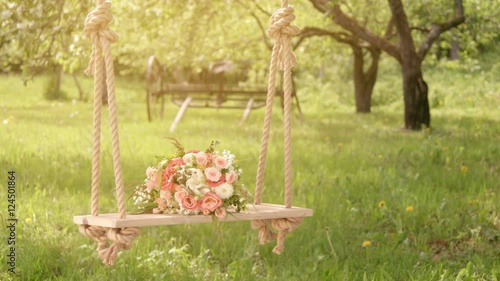 Flowers on wooden swing under blossoming apple trees, sun flare