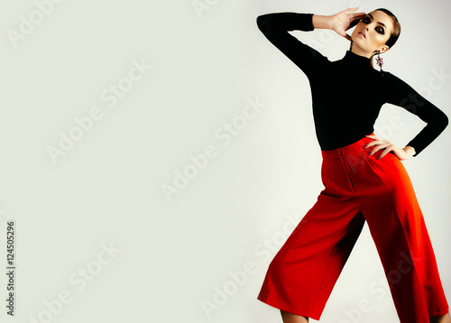 beautiful brunette girl with shiny skin, make-up, smoky eyes and pricheskoy.Poziruet in black jacket and red pants in the studio on a white background. Advertising Space photo