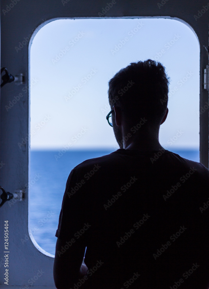 Silhouette of man with the glasses looking through the window at the sea