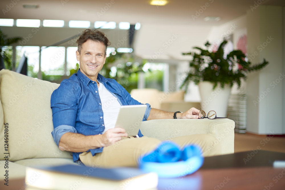 Shot of a smiling confident man using his tablet while relaxing on the sofa at home. Shot of a smiling confident man using his tablet while relaxing on the sofa at home.