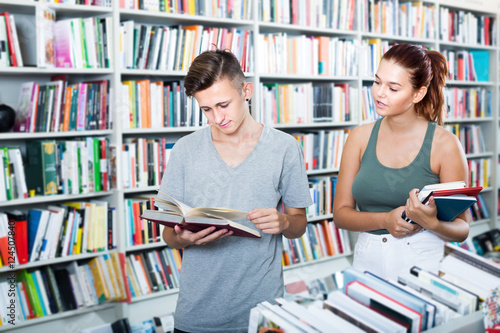 Two teenagers reading book together in book store