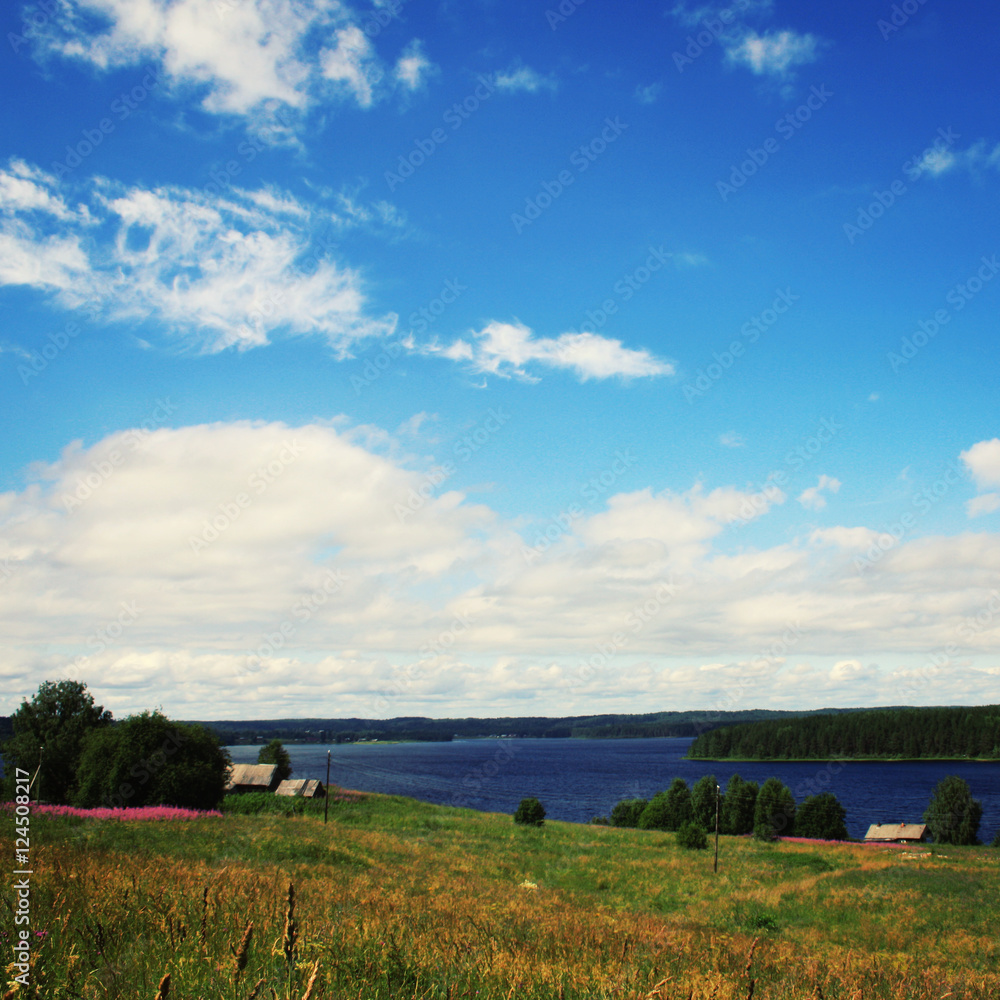 Small village near Kenozero lake. View from the hill. Summertime meadows. Suny summer day. Journey to the north of Russia. Kenozersky National Park (UNESCO Biosphere Reserve). Small village near Kenozero lake. View from the hill. Summertime meadows. Suny summer day. Journey to the north of Russia. Kenozersky National Park (UNESCO Biosphere Reserve).