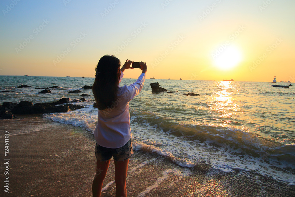 asia woman tourist taking photo on sea beach with mobile smart phone camera at sunset asia woman tourist taking photo on sea beach with mobile smart phone camera at sunset