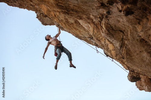 Male rock climber hanging with one hand on on a cliff 