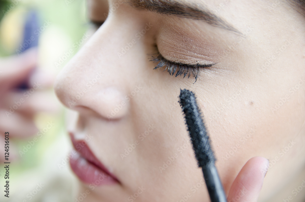 Woman applied eyeliner by makeup artist, outside the garden. Makeup artist apply eyeliner on the clients eyes