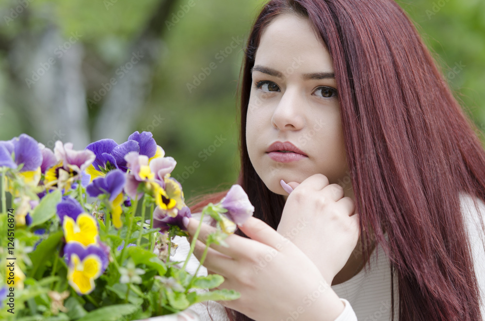 Cute redhair sitting on a wooden garden table, pot with flowers. Head on hands facing the camera