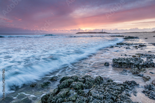 Last lights at Cape Trafalgar with waves crashing on the rocks and lighthouse of Trafalgar in the background, Cadiz, Spain photo