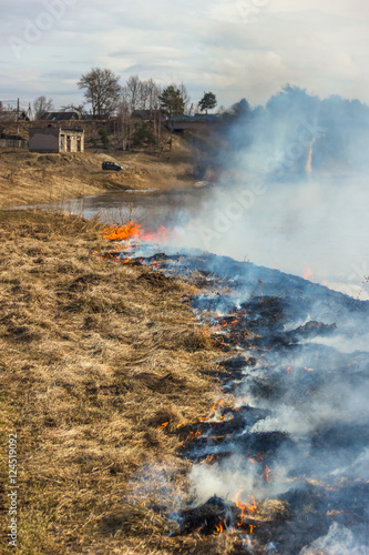 Burning dry grass on the river bank. Spring. Near the village.