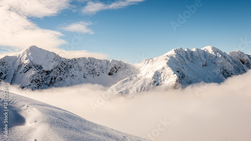mountain tops in winter covered in snow with bright sun and blue © Martins Vanags