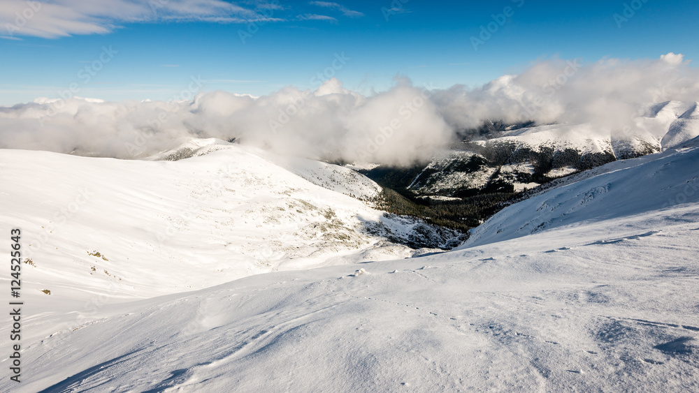 Obraz premium mountain tops in winter covered in snow with bright sun and blue