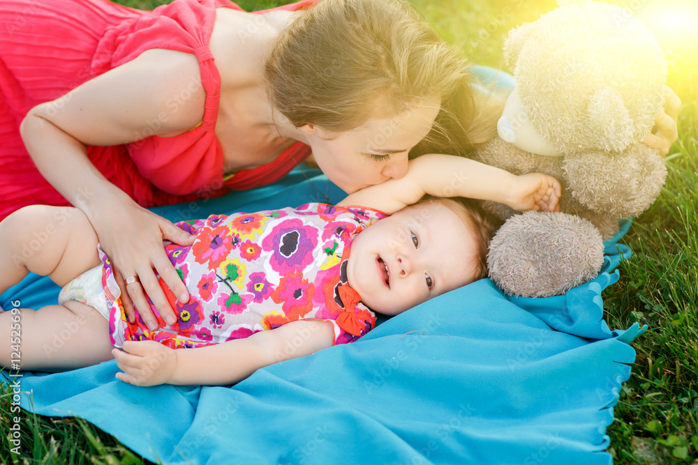 Young woman kissing little girl lying on blue rug Young woman kissing little girl lying on blue rug