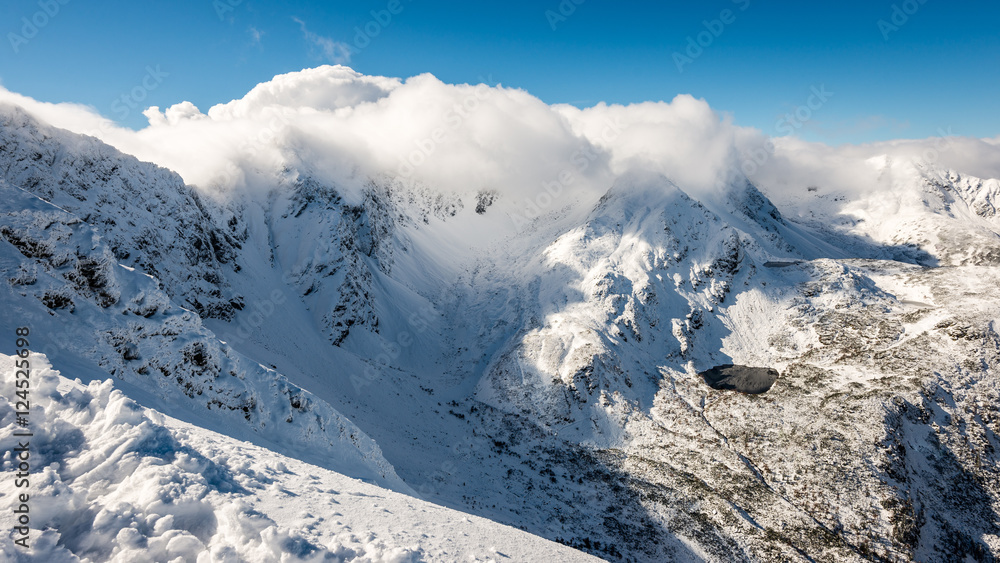 Obraz premium mountain tops in winter covered in snow with bright sun and blue