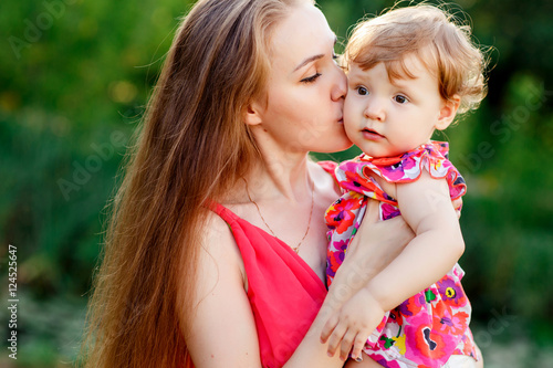 Young mother kissing baby daughter in park