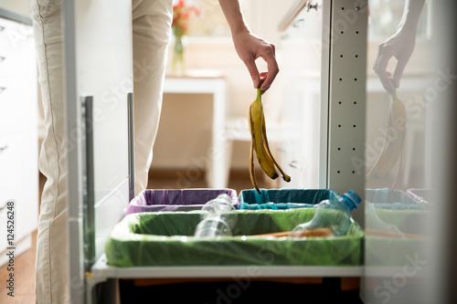 Obraz na plátně Woman putting banana peel in recycling bio bin in the kitchen