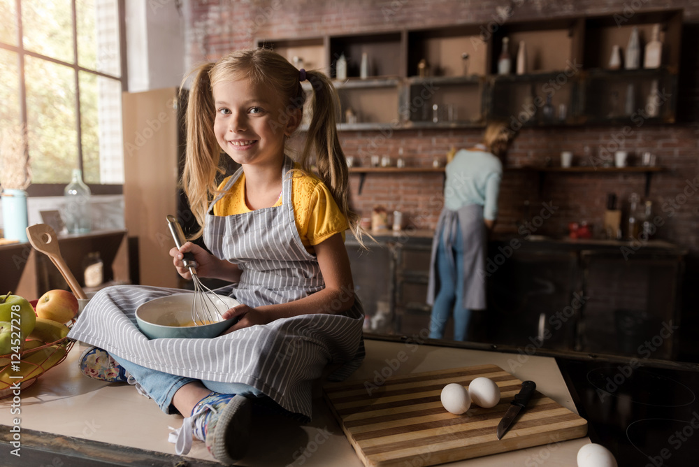 Smiling amused girl mixing eggs sitting on the table Smiling amused girl mixing eggs sitting on the table