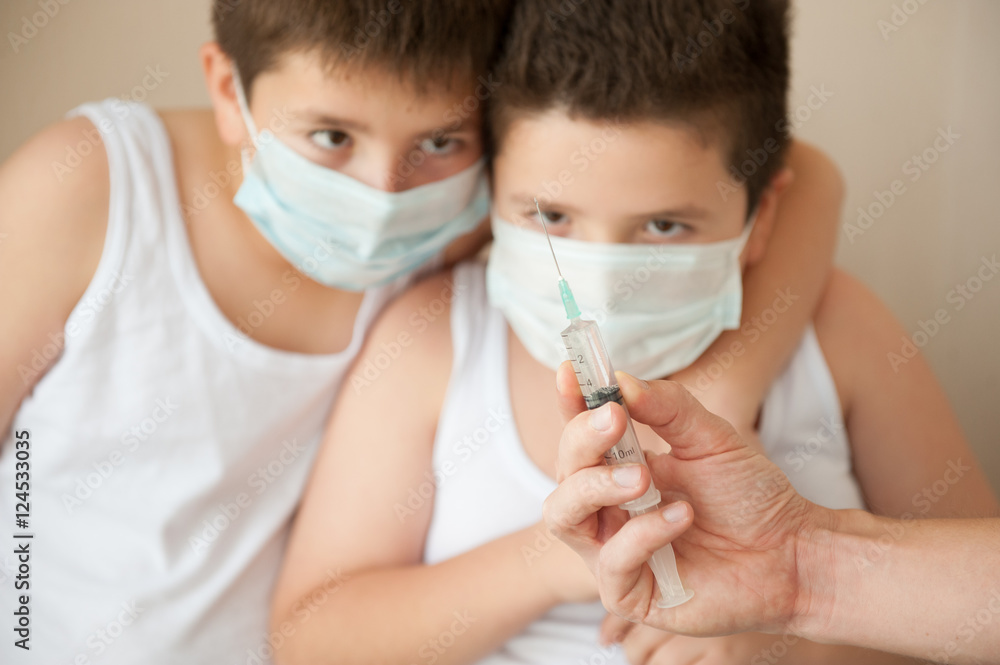 two boys in surgical mask looking at the hand with syringe