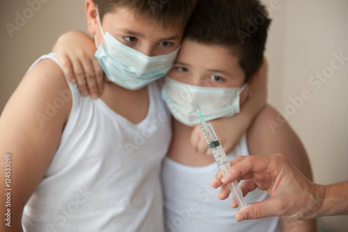 two scared brothers in medical mask looking at hand with syringe