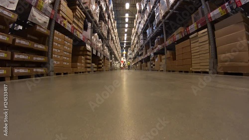 Wallpaper Mural Funny Young Girl in mini skirt rides shopping cart forward to camera in furniture warehouse store between rows of shelves with cardboard boxes Torontodigital.ca