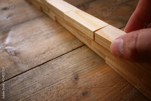 male hand building brick wall from wooden domino blocks