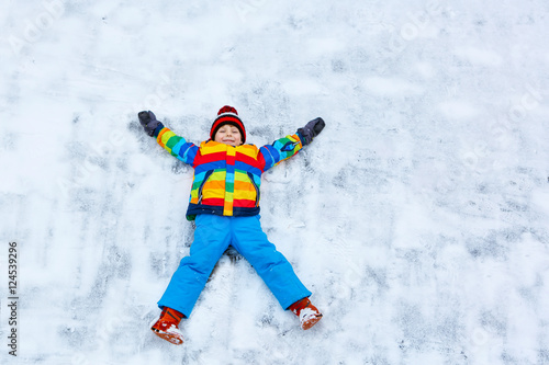 Little kid boy making snow angel in winter, outdoors