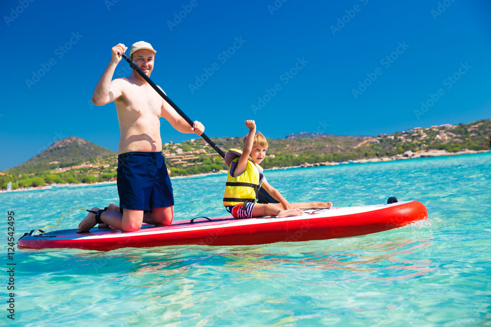 Father with his little happy son having fun on stand up paddle board on Santa Gulia beach, Corsica, France, Europe