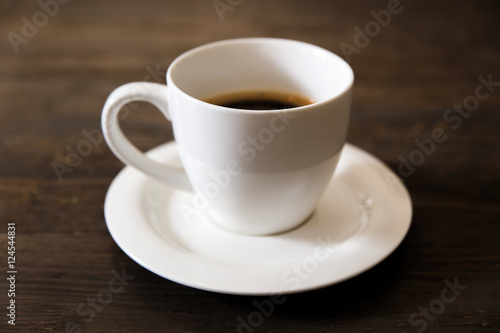 A white cup of black coffee on the wooden table. Selective focus, small depth of fieild.