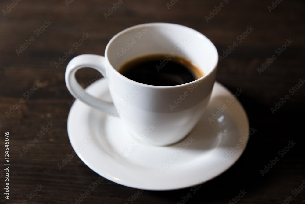 A white cup of black coffee on the wooden table. Selective focus, small depth of fieild. A white cup of black coffee on the wooden table. Selective focus, small depth of fieild.