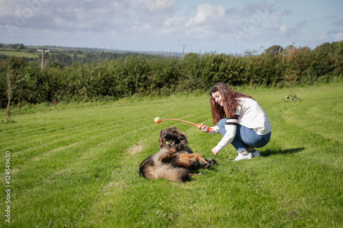 Teenage girl plays with her dog outside in a field, he is rolling over