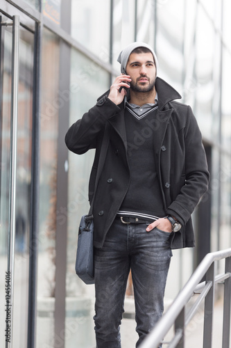 Young businessman portrayed in front of the modern office building and talking on the phone.