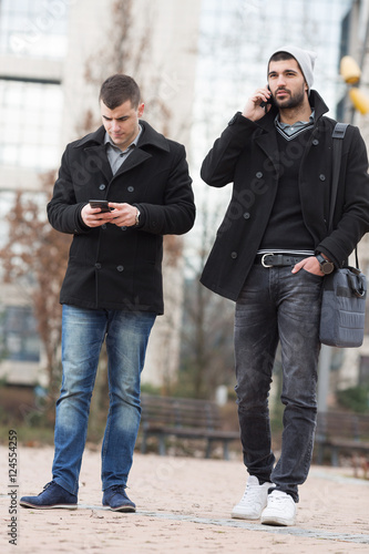 Two young businessmen portrayed whie using their phones.