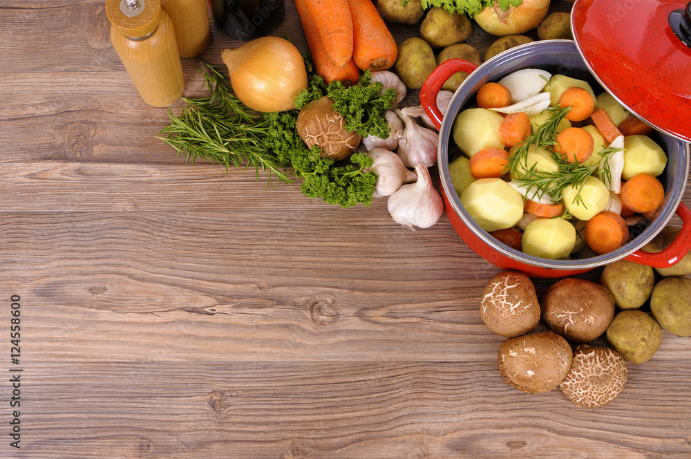 Red casserole dish stew pot or dutch oven with winter vegetables and herbs for soup on wood kitchen counter worktop photo Red casserole dish stew pot or dutch oven with winter vegetables and herbs for soup on wood kitchen counter worktop photo