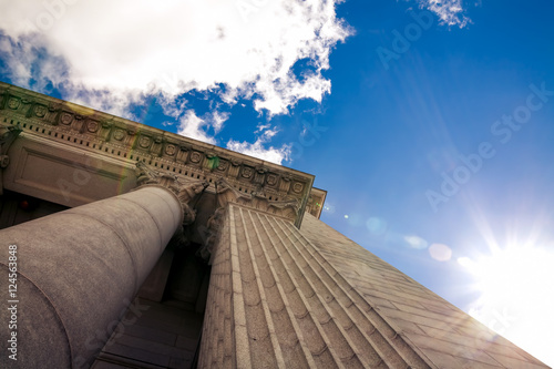 Upward view of a court house with impressive pillars. Morning sun shining down creating a beautiful lens flare. Architectural, construction, law, education and career concept