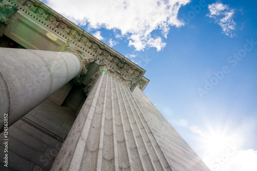Upward view of a court house with impressive pillars. Morning sun shining down creating a beautiful lens flare. Architectural, construction, law, education and career concept