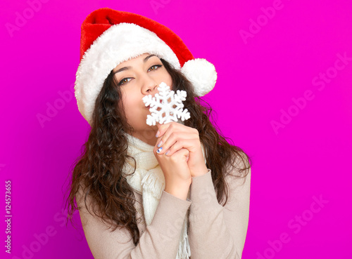 girl in santa hat portrait with big snowflake toy posing on pink color background  christmas holiday concept  happy and emotions