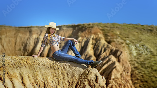 Foto Young beautiful girl in cowboy clothes sitting on the edge of the grand canyon