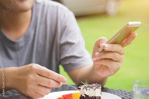 A man eating a cake and playing smartphone,outdoor cafe and vint