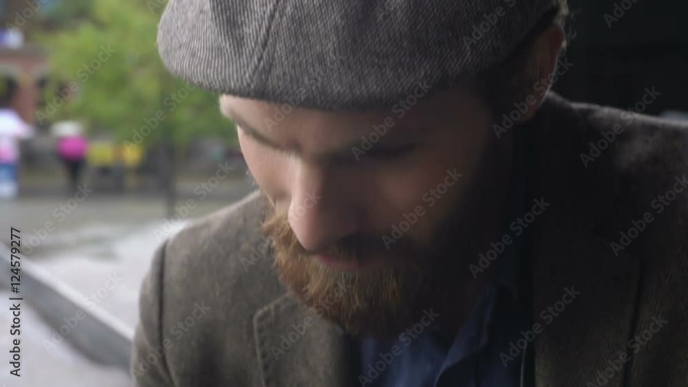 Close up with tilt up of young man with beard sitting outside on nice chilly day and typing something on mobile phone Close up with tilt up of young man with beard sitting outside on nice chilly day and typing something on mobile phone