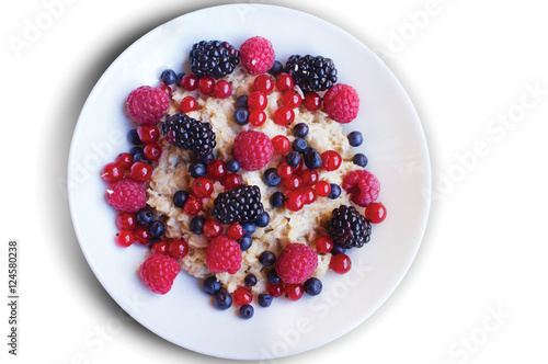 Oatmeal with raspberries, blackberries, red currant and blueberries in a white plate on white background photo