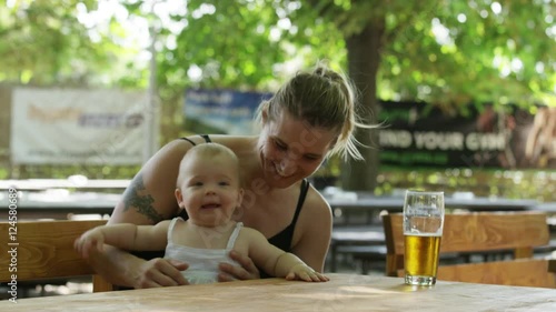 A mother sits in a beer garden with her baby on her lap.  The baby girl is shaking her head. 4k. photo