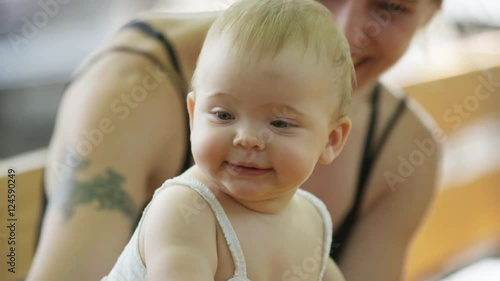 A baby looks at the camera while her mother smilles in the background.  The mother waves at the camera. 4k. photo